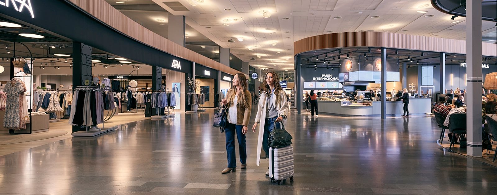 Två kvinnor med resväskor som shoppar på Marknadsplatsen, Arlanda, innan avgång.