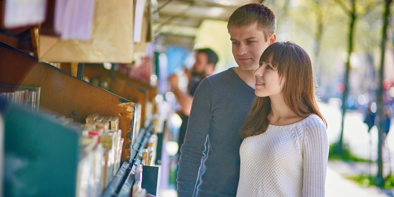 Romantic couple in Paris selecting a book from a bookseller near the Seine